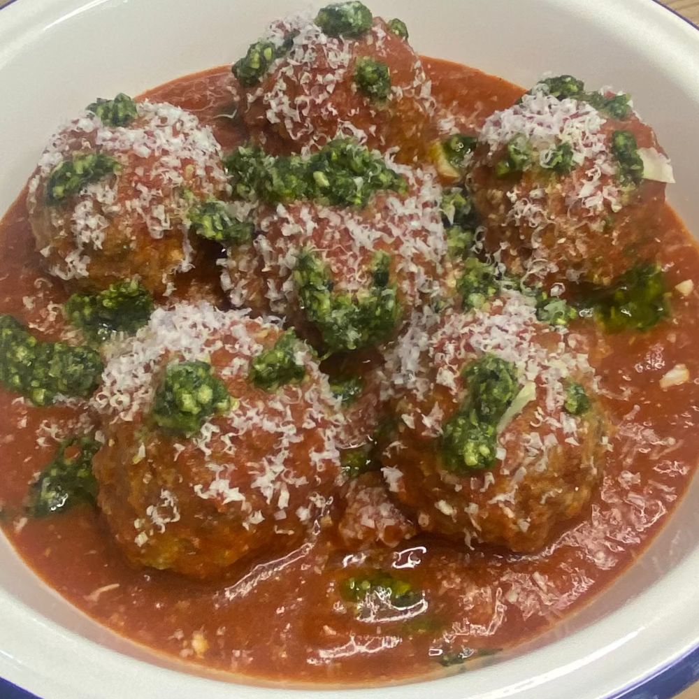 Bowl of meatballs in tomato sauce with basil pesto and parmesan on a wooden table