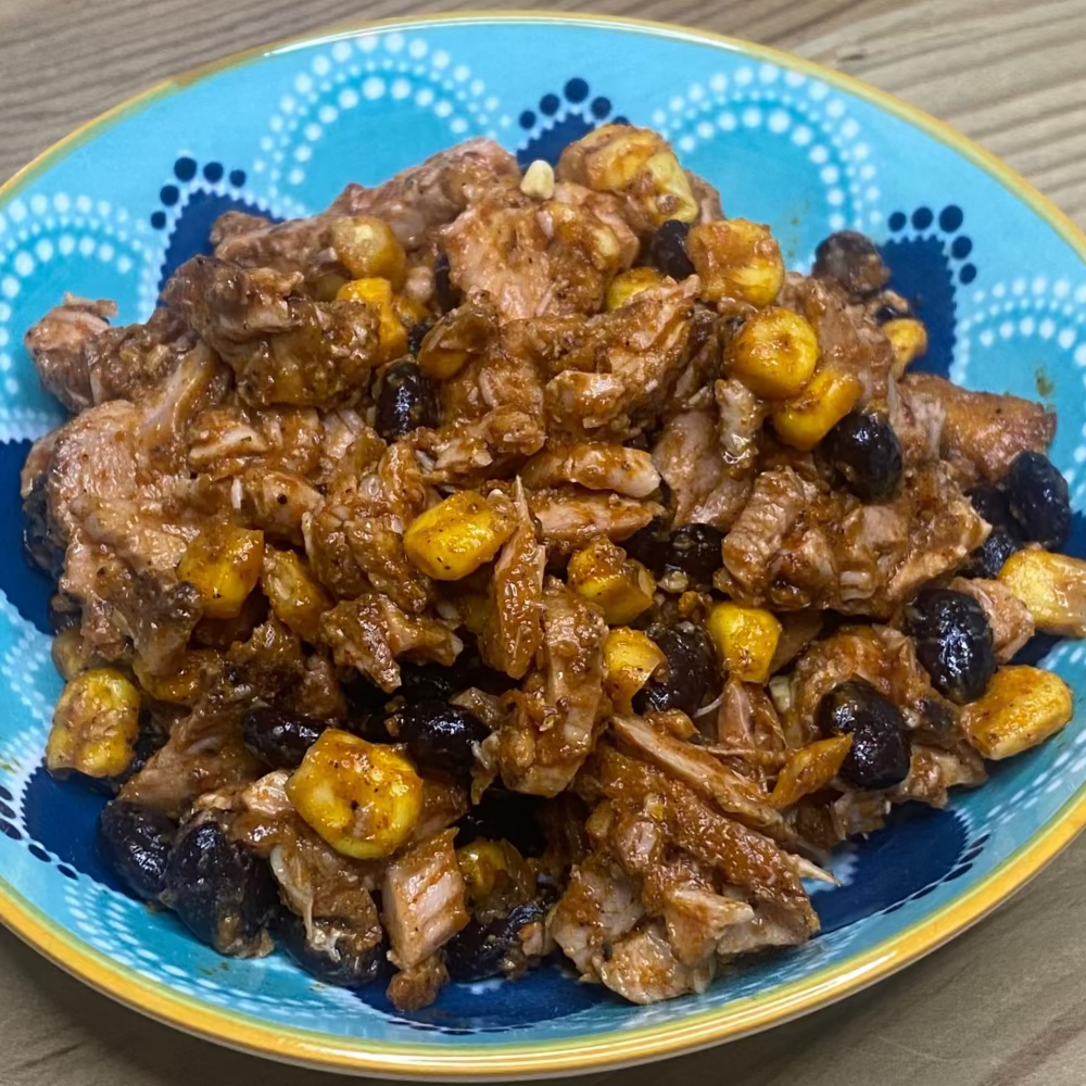 Mexican chicken with achiote avocado, lime, jalapenos, and cilantro on a wooden board with sweetcorn and beans.