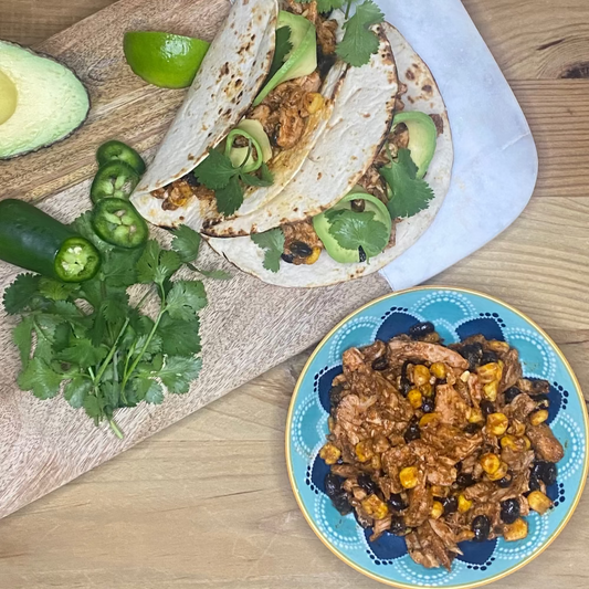 Mexican chicken Tacos with achiote  avocado, lime, jalapenos, and cilantro on a wooden board with sweetcorn and beans.