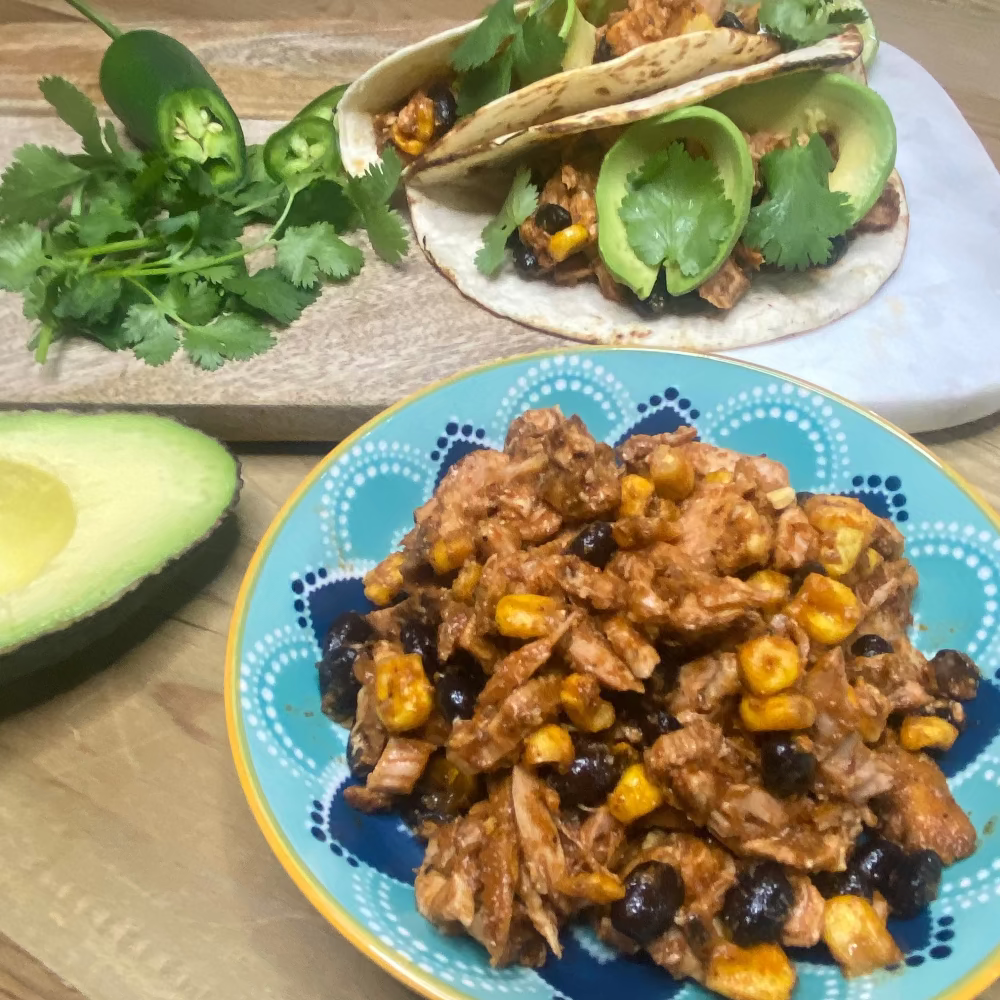 Mexican chicken Tacos with achiote  avocado, lime, jalapenos, and cilantro on a wooden board with sweetcorn and beans.