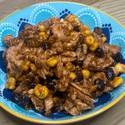 Mexican chicken with achiote  avocado, lime, jalapenos, and cilantro on a wooden board with sweetcorn and beans.